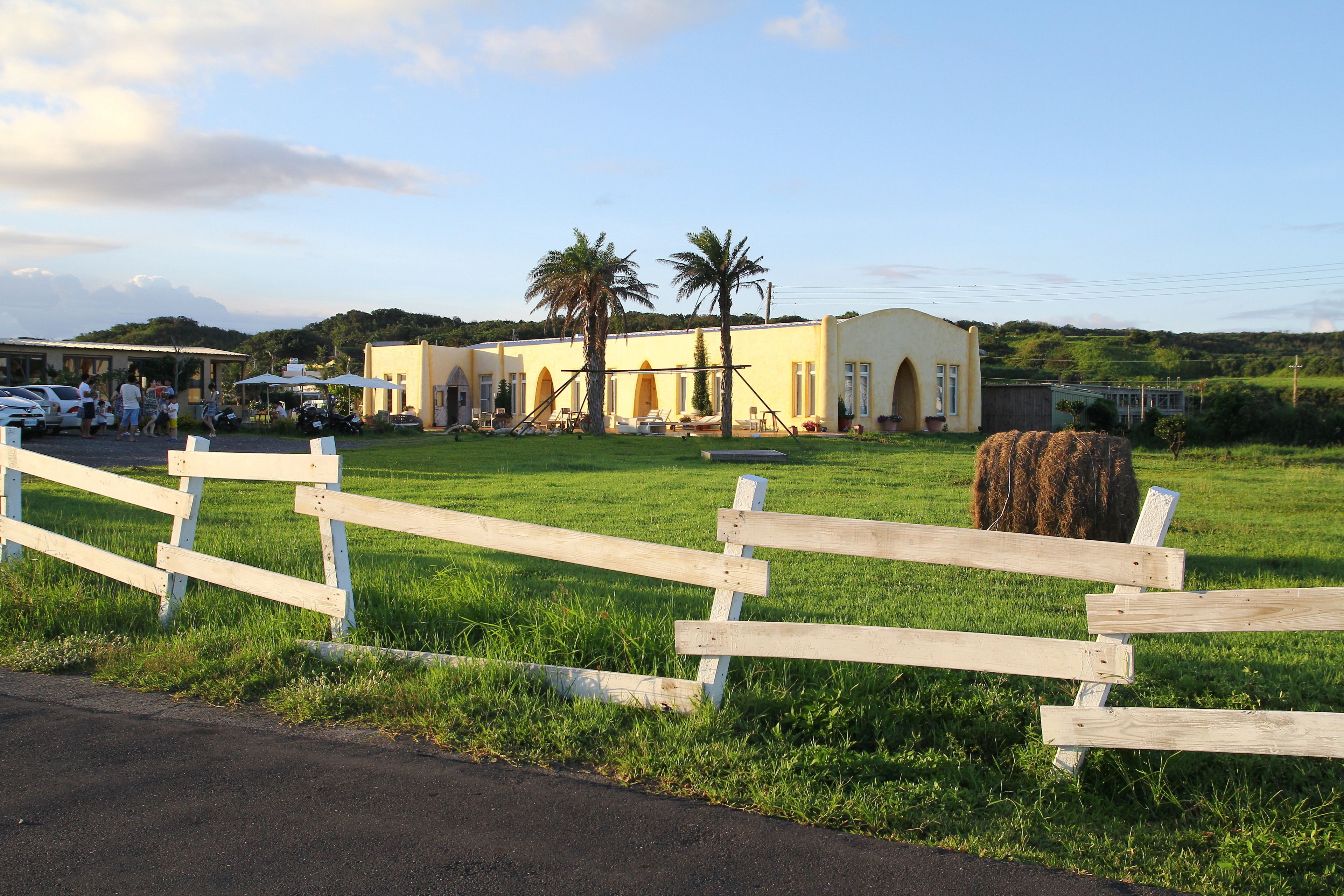 A fenced grassy area with a building featuring arched windows and a yellow facade.