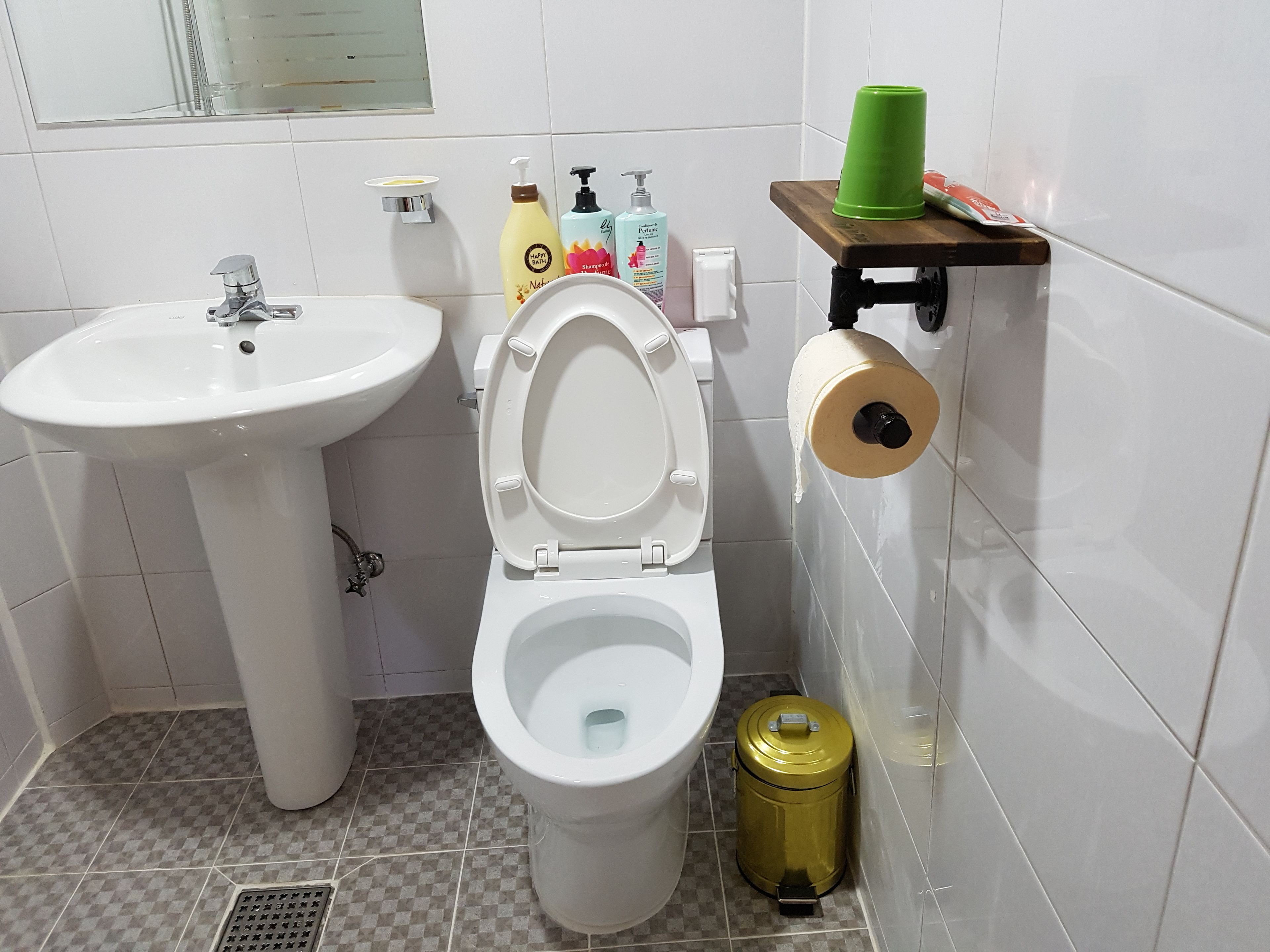 A bathroom with a white sink, toilet, and a green trash bin.