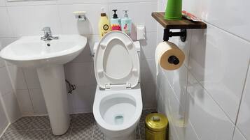 A bathroom with a white sink, toilet, and a green trash bin.