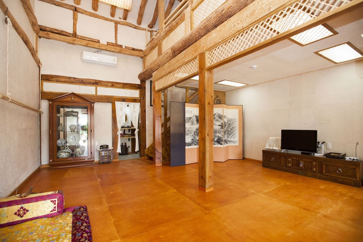 A spacious living room with a wooden ceiling, a television on a wooden cabinet, and a traditional Japanese sliding door.