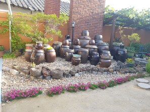 A courtyard with large ceramic pots arranged in a tiered display, surrounded by a gravel path and flowering plants. - The Hanok (Jeonju)