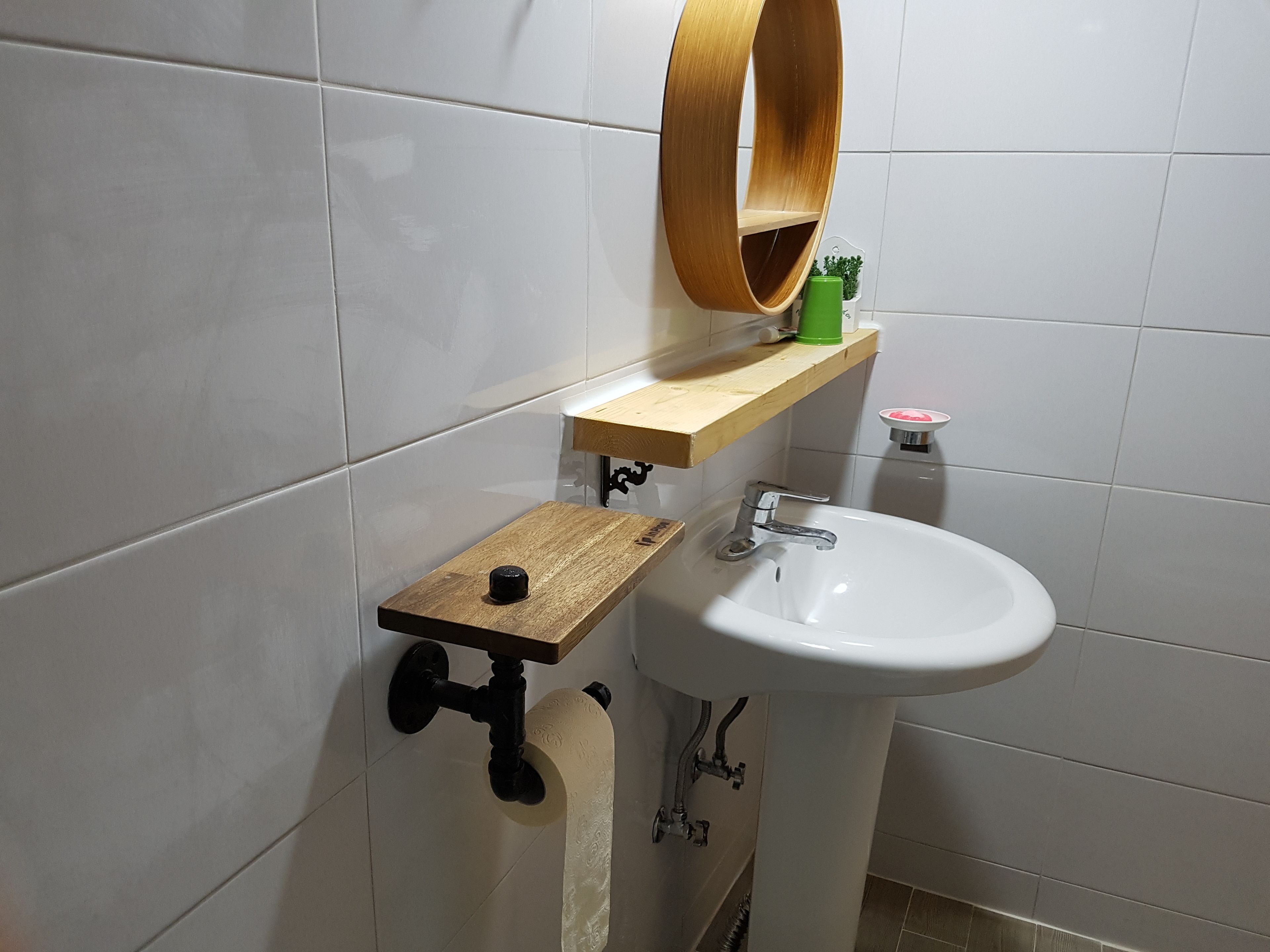 Un baño con un lavamanos blanco, un estante de madera, un espejo y un dispensador de papel higiénico.