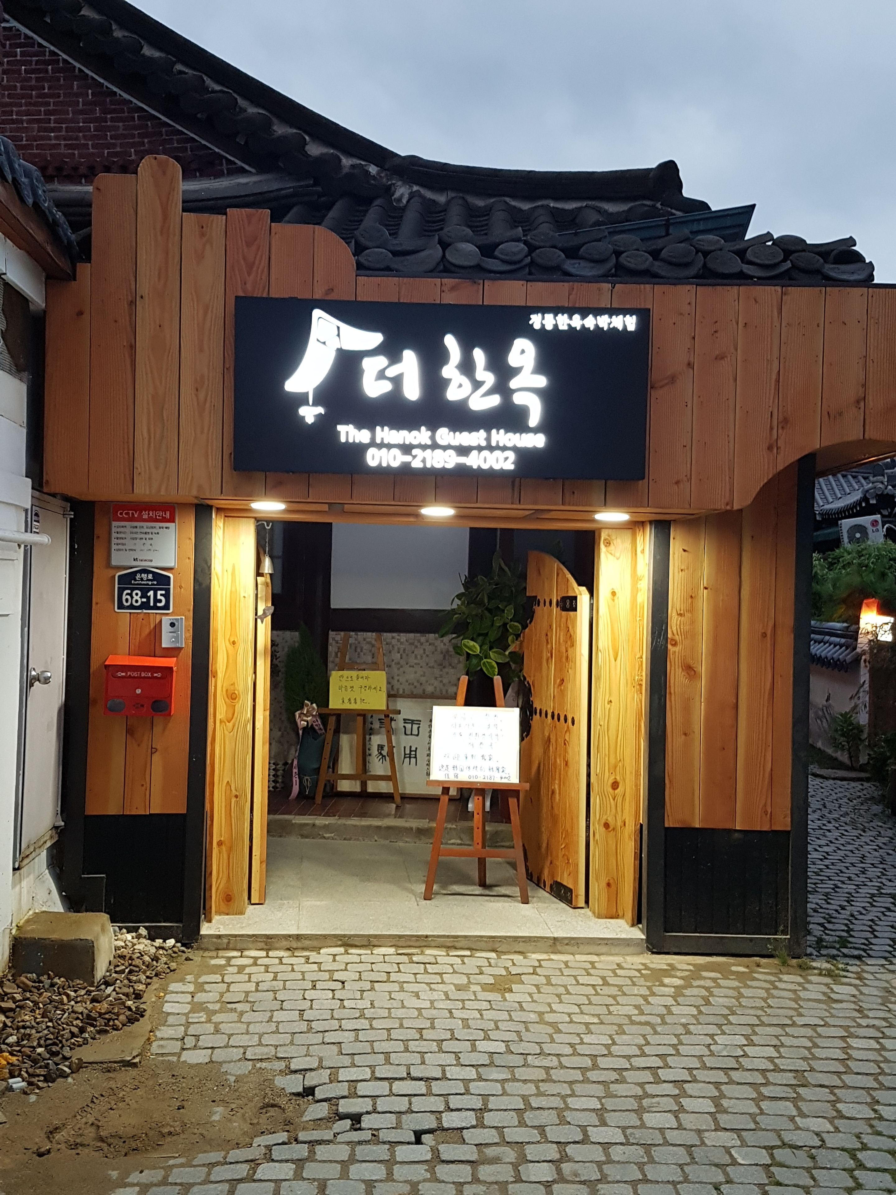 A traditional wooden building with a sign reading "The Hanok Guest House" and a contact number.