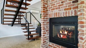 A modern interior with a staircase, a fireplace, and a brick wall.