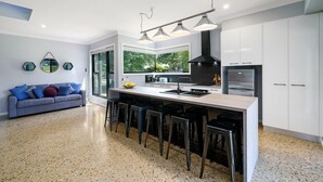 A modern kitchen with a central island, bar stools, and a large window offering a view of greenery.