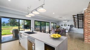 A modern kitchen with a large island, a dishwasher, and a sink. There is a dining area with a table and chairs, and a brick wall.