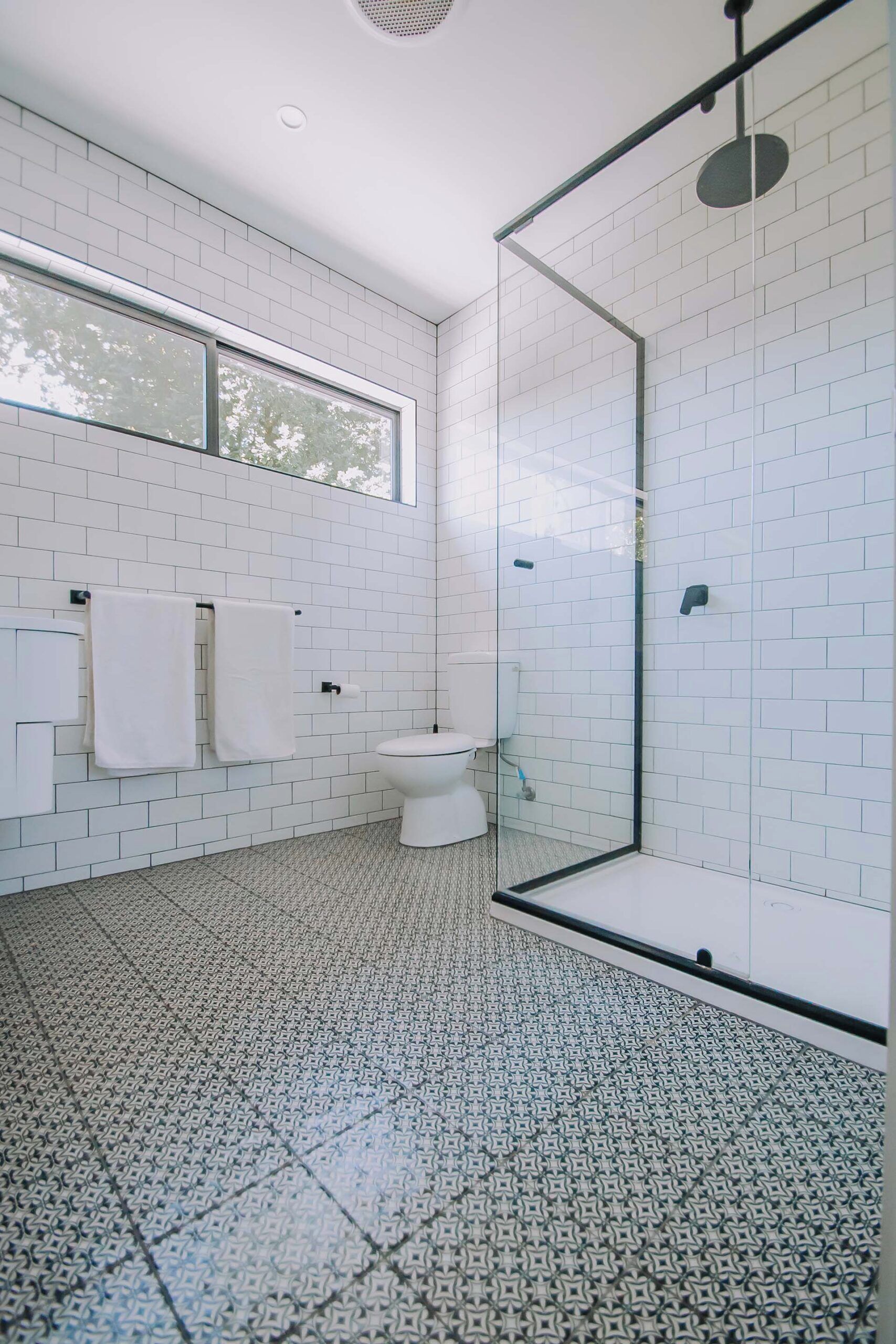 A modern bathroom with white subway tiles, a glass shower enclosure, a toilet, and a window providing natural light.