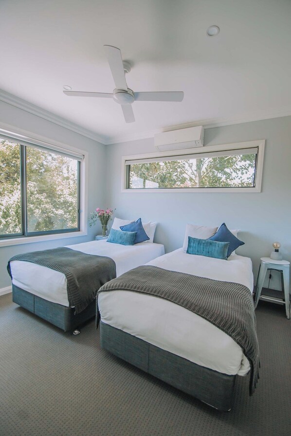 A hotel room with two beds, a ceiling fan, a window with a view of trees, and a small bedside table with a lamp. - Lusso (Whitfield)
