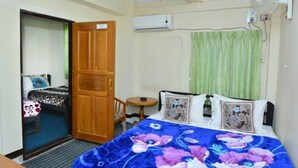 A hotel room with a bed, a wooden wardrobe, a small table, and an air conditioning unit.