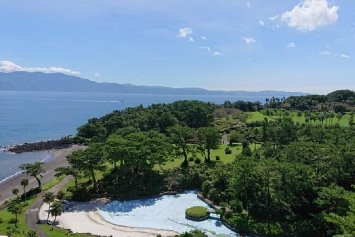 Un paysage côtier avec une plage, une végétation luxuriante et une vue sur la mer et les montagnes lointaines.