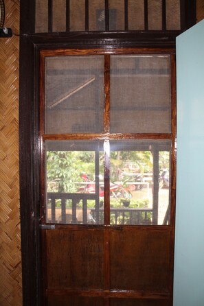 A wooden door with a screen window, a herringbone-patterned wall, and a view of an outdoor area with a fence and greenery. - Cliffside Cottages (El Nido)