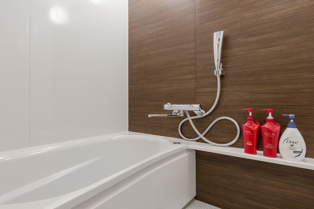 A modern bathroom with a white bathtub, a shower with a handheld showerhead, and a shelf with three bottles of Dove body wash.