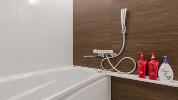 A modern bathroom with a white bathtub, a shower with a handheld showerhead, and a shelf with three bottles of Dove body wash.