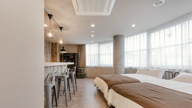 Une chambre d’hôtel moderne dotée d’un grand lit, d’un bureau avec des tabourets de bar et d’une grande fenêtre laissant entrer la lumière naturelle.