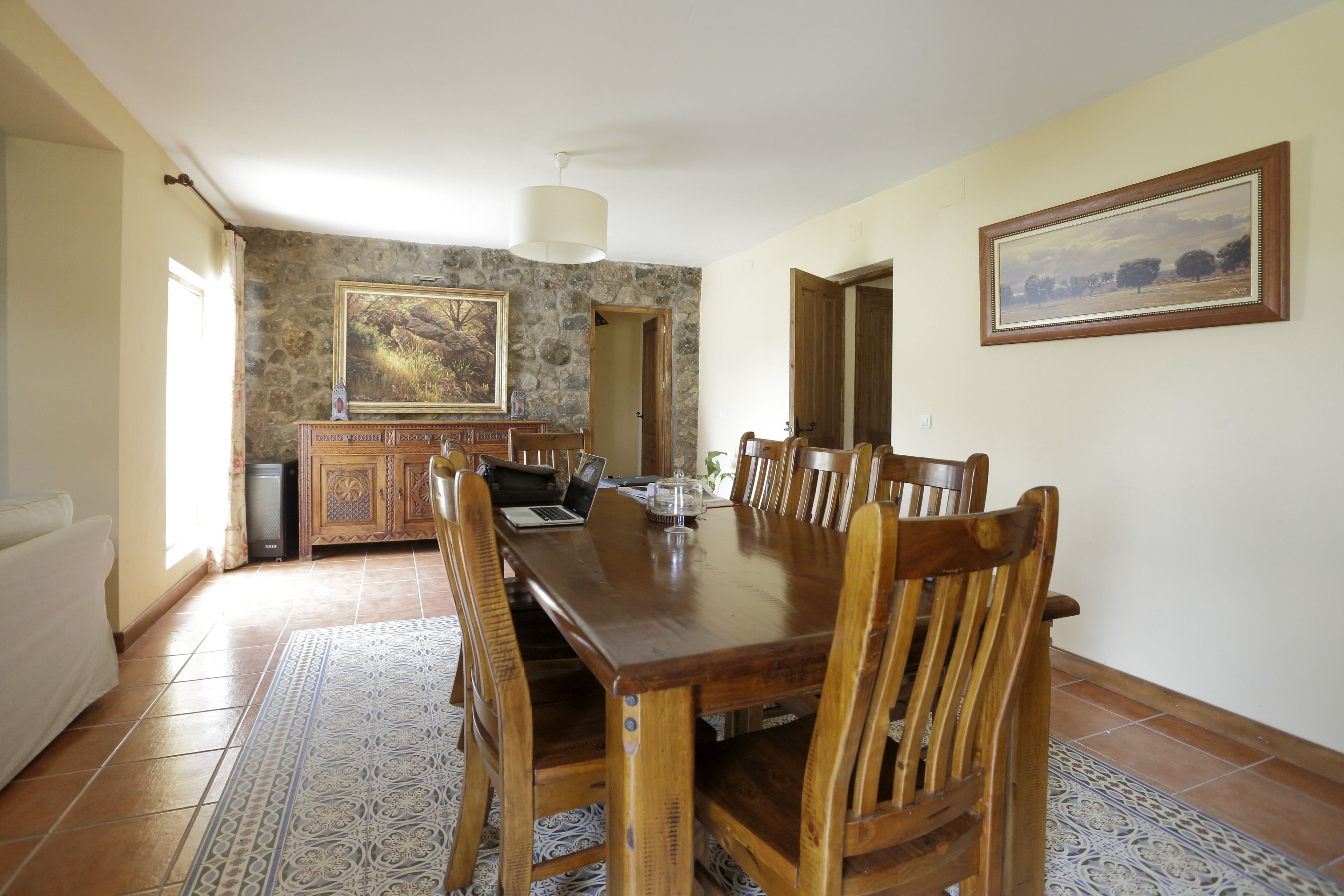 Un coin repas avec une table et des chaises en bois, un ordinateur portable et un tableau accroché au mur.