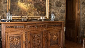 Un aparador de madera con intrincados grabados, un cuadro enmarco de un paisaje forestal y faroles decorativos.