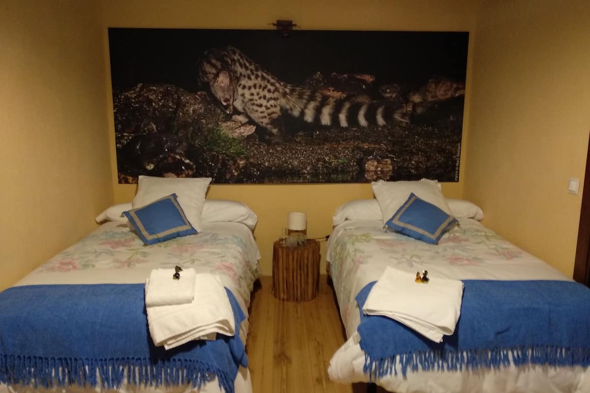A hotel room with two beds, each with a floral bedspread and blue pillows. There is a painting of a leopard on the wall above the beds.