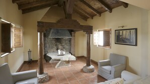 Una habitación rústica con chimenea de piedra, vigas de madera y un sillón a cuadros.