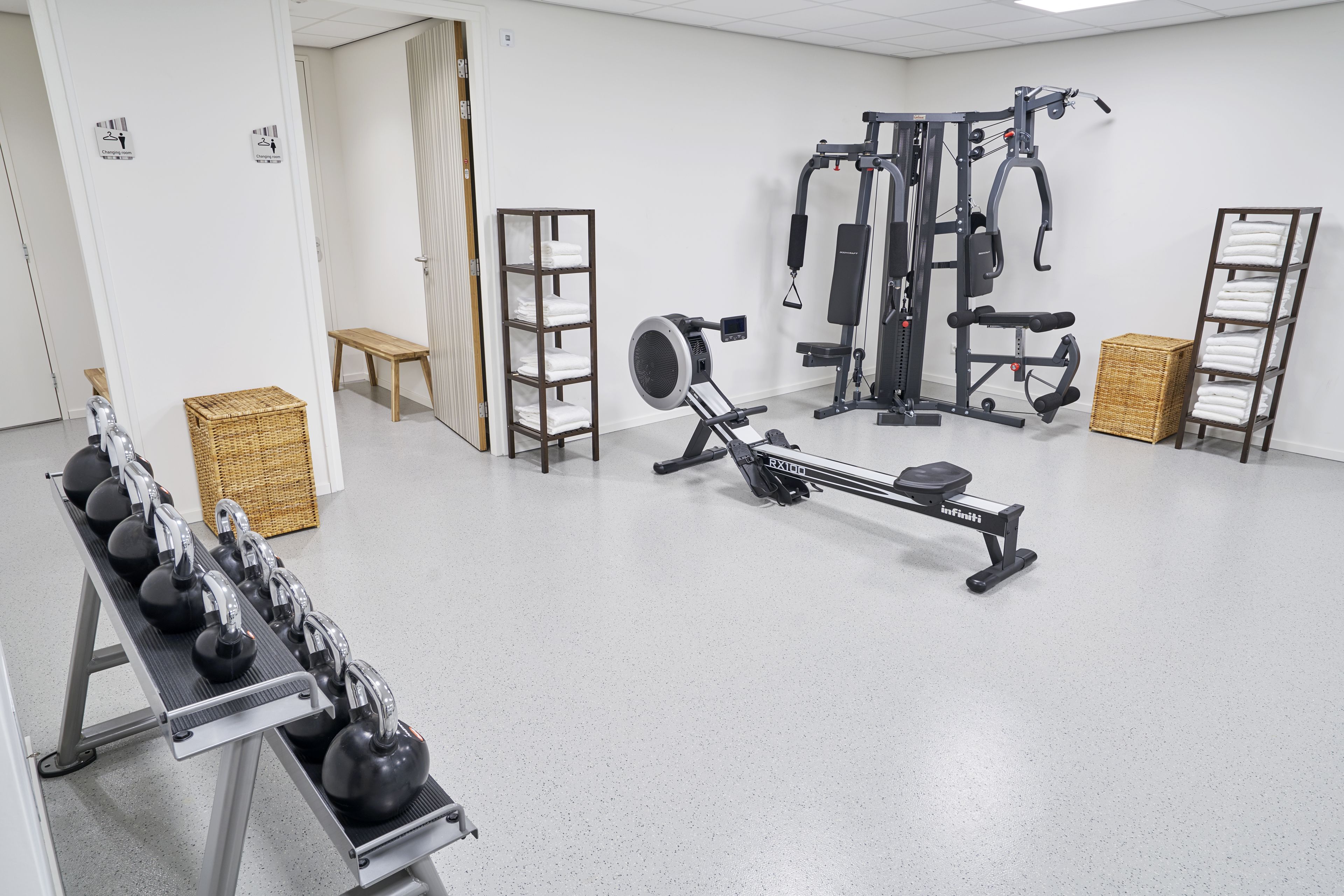 Un gimnasio con equipamiento de ejercicio, una banca y un estante de toallas.