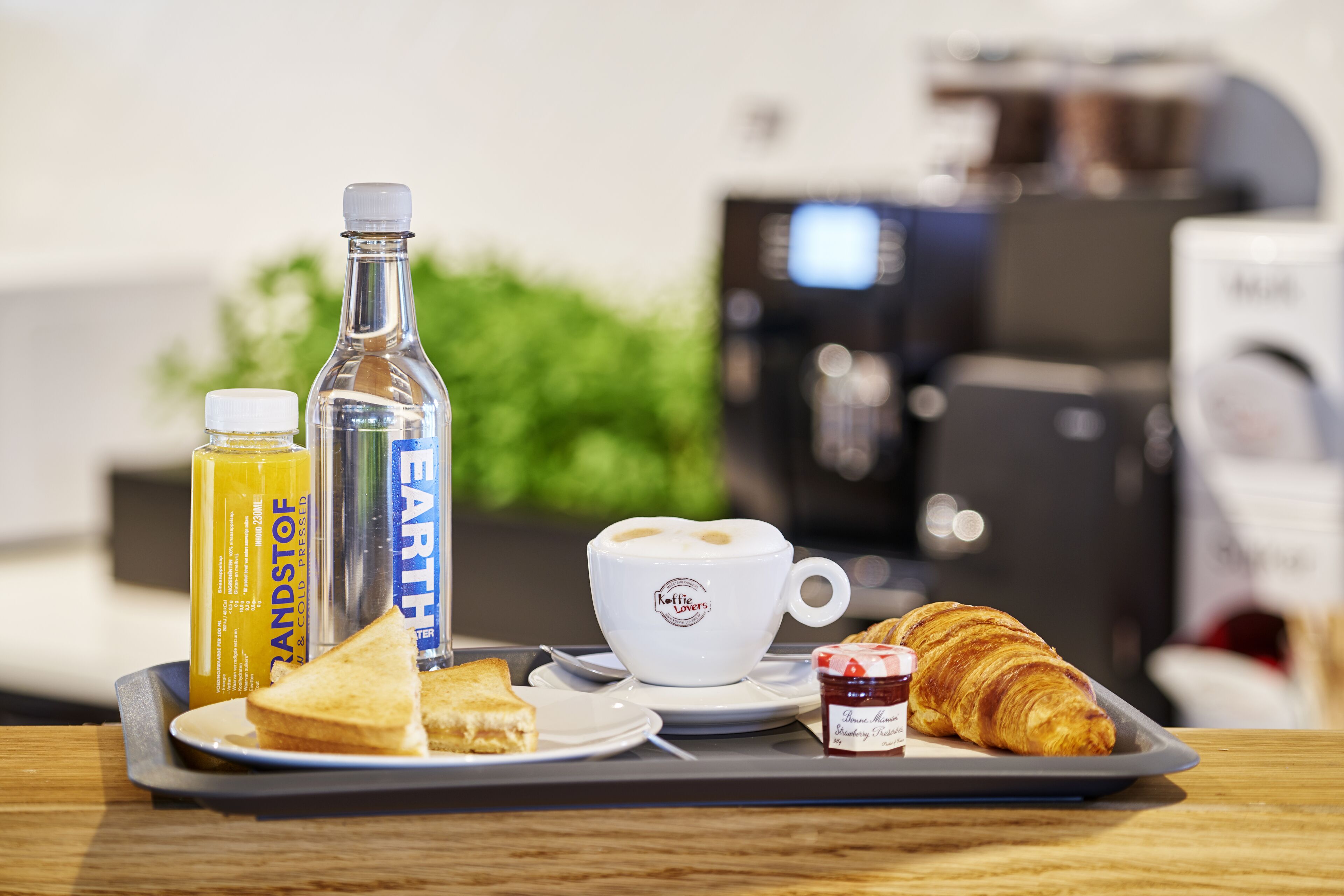 A breakfast tray with a croissant, a sandwich, a cup of coffee, and two bottles of juice.