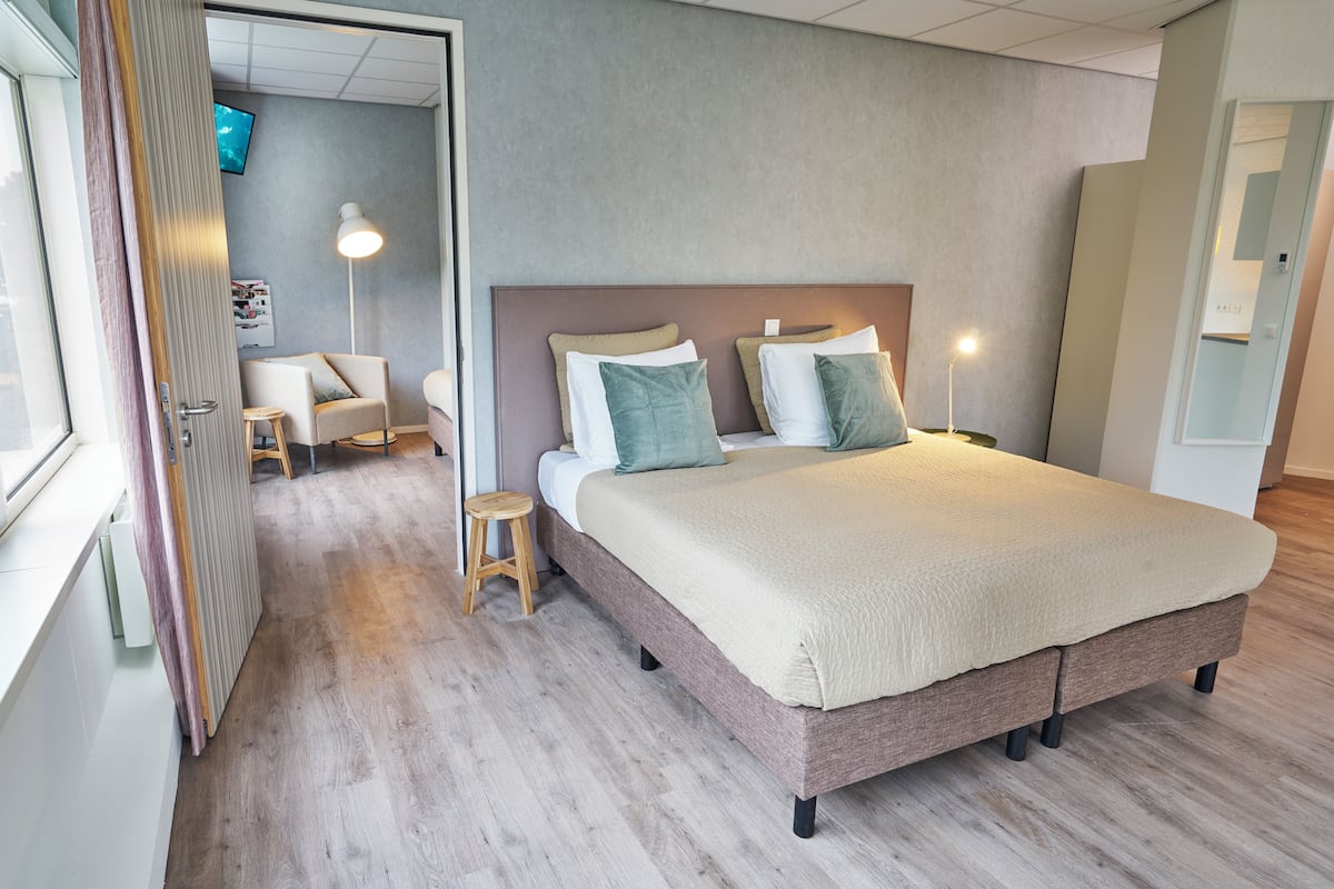 Un dormitorio moderno con una cama grande, lámparas de noche y un pequeño taburete.