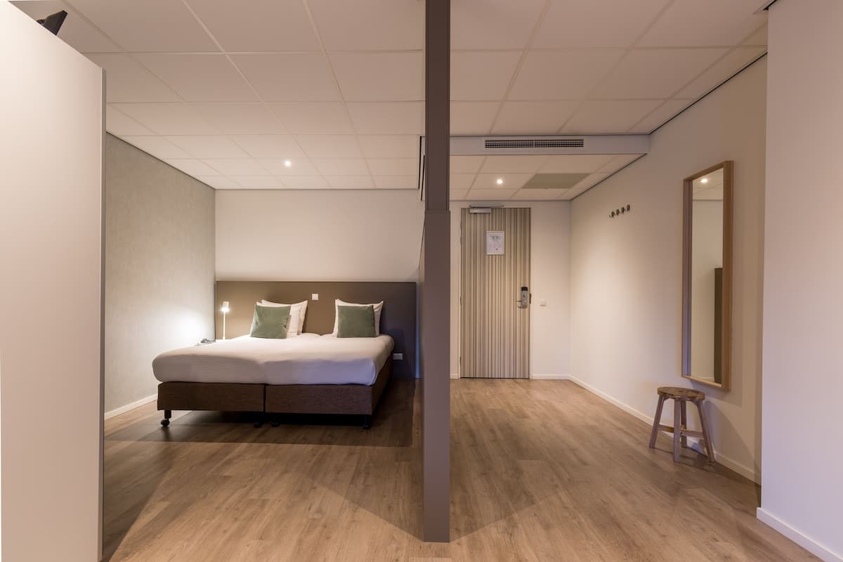 Un dormitorio con cama, taburete, espejo y puerta.