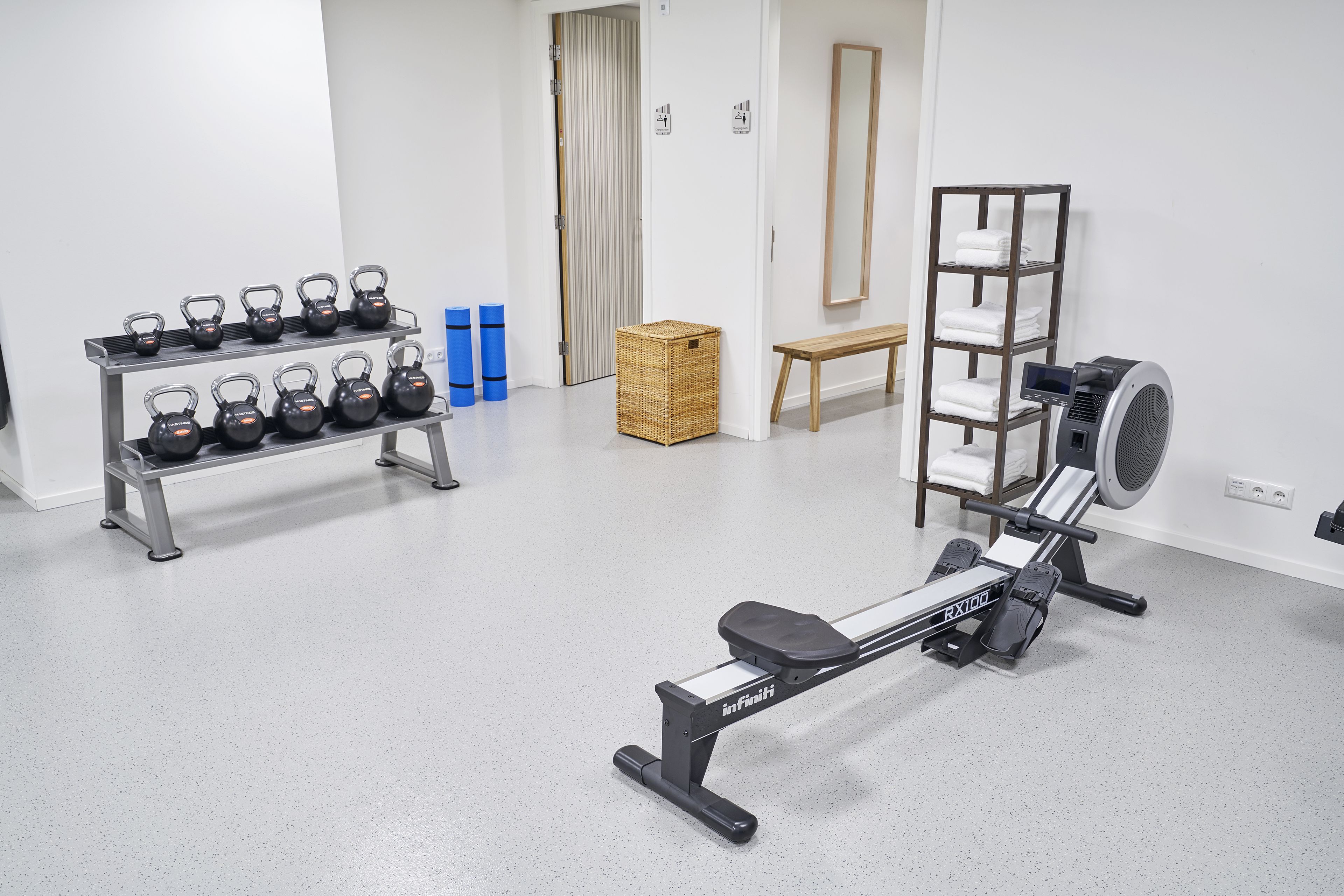 Un gimnasio con equipo de ejercicio, incluyendo pesas rusas, mancuernas y una máquina de remo.