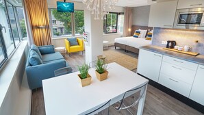 Ein modernes Hotelzimmer mit einem großen Bett, einem Esstisch, einer Küchenzeile und einer Sitzecke mit Sofa und Sesseln.