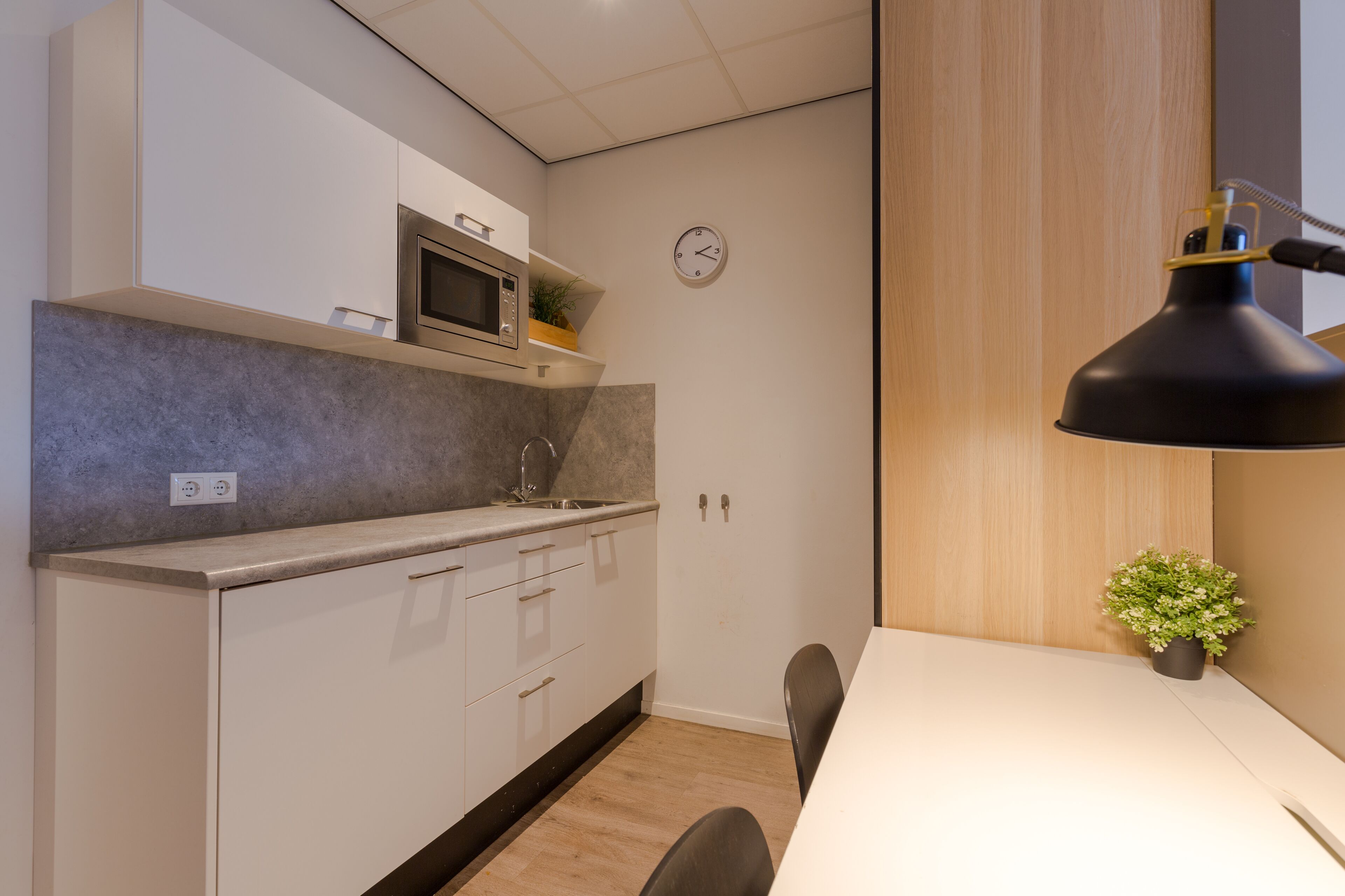 A modern kitchen with white cabinets, a microwave, and a clock on the wall.