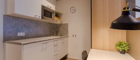 A modern kitchen with white cabinets, a microwave, and a clock on the wall.