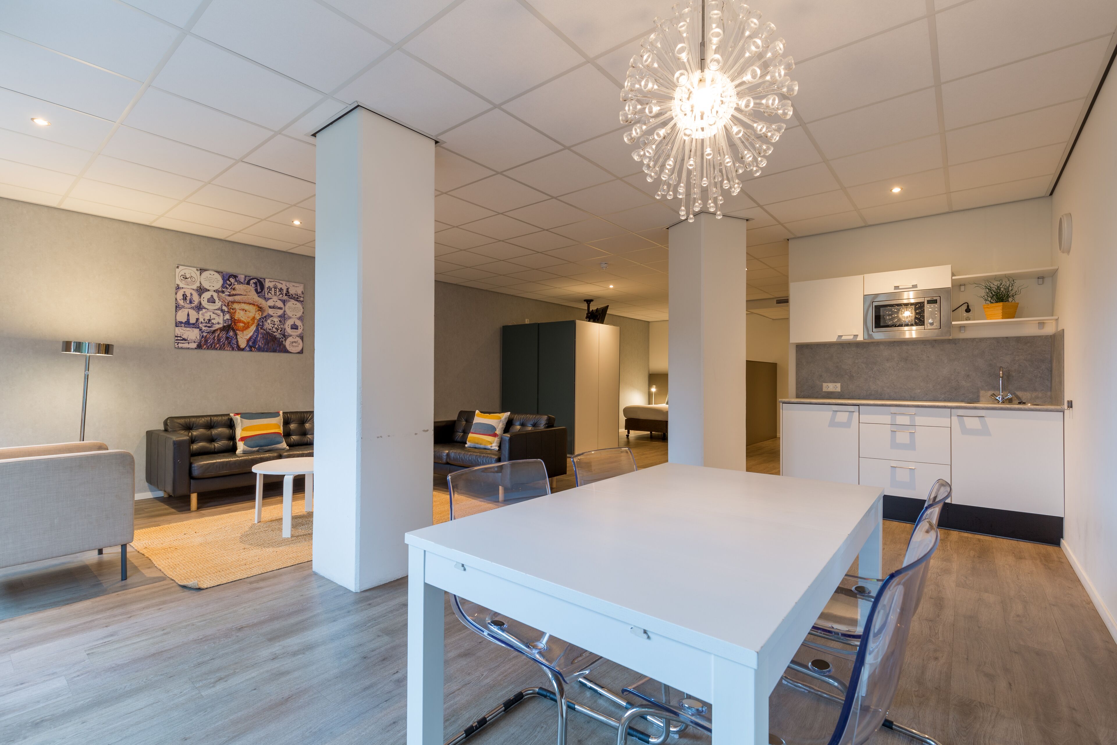 A modern living room with a white dining table, grey sofas, and a large chandelier.