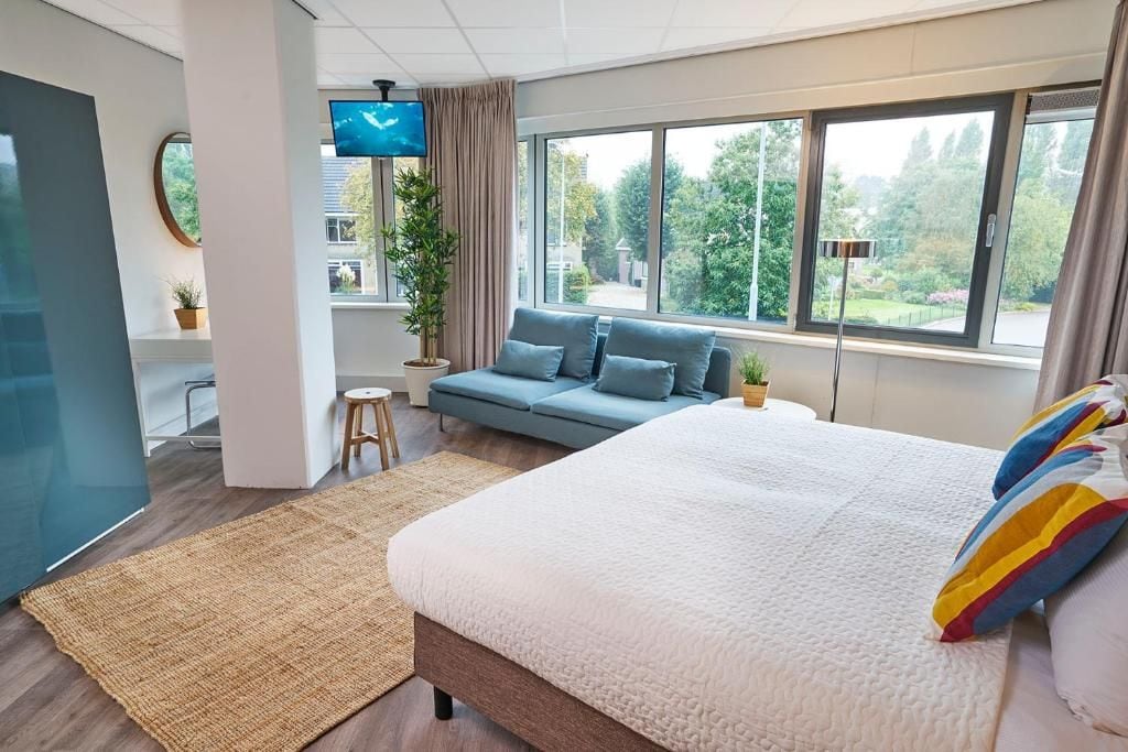A modern bedroom with a large bed, a sofa, a TV, and a view of the outdoors.