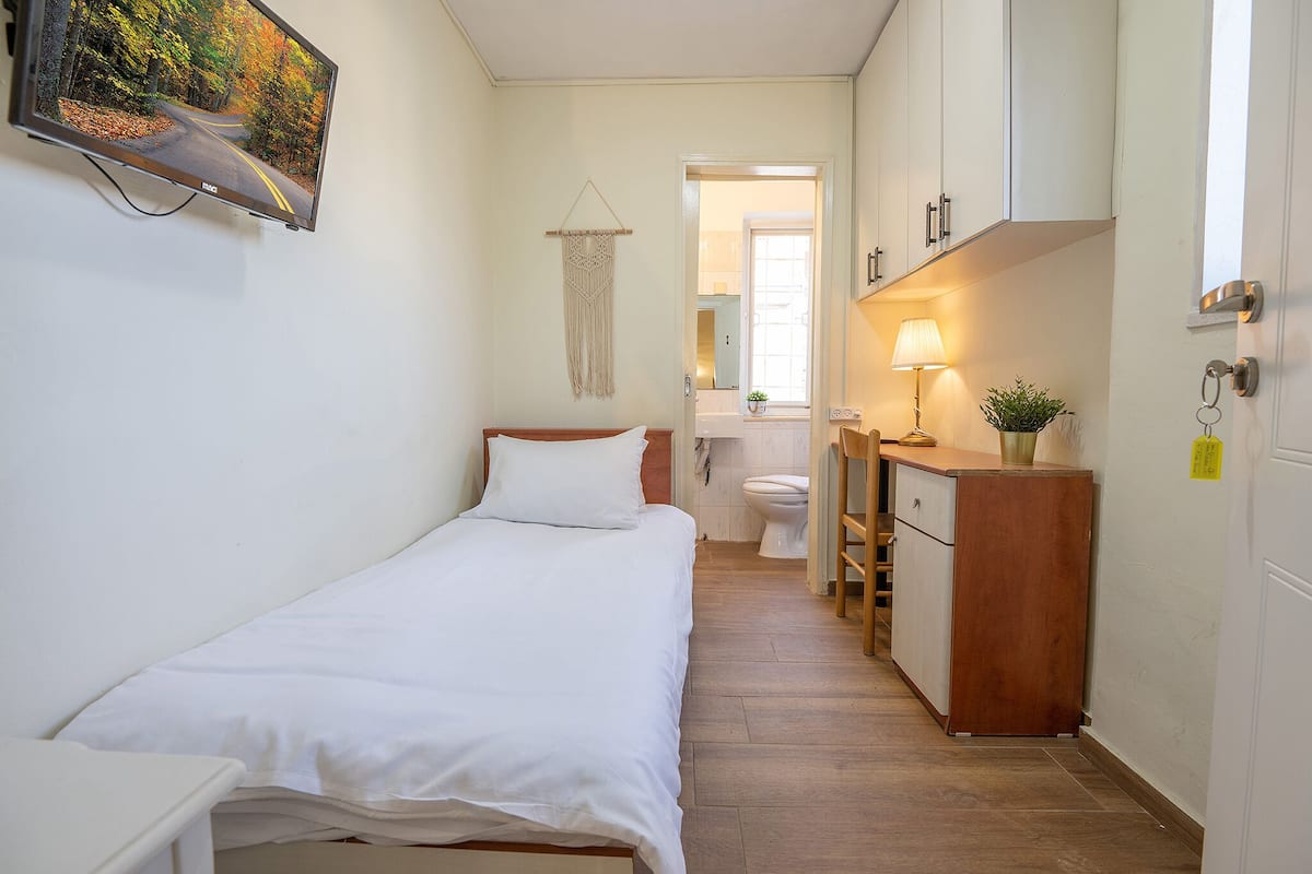 A small, clean room with a bed, a desk, a toilet, and a mirror.