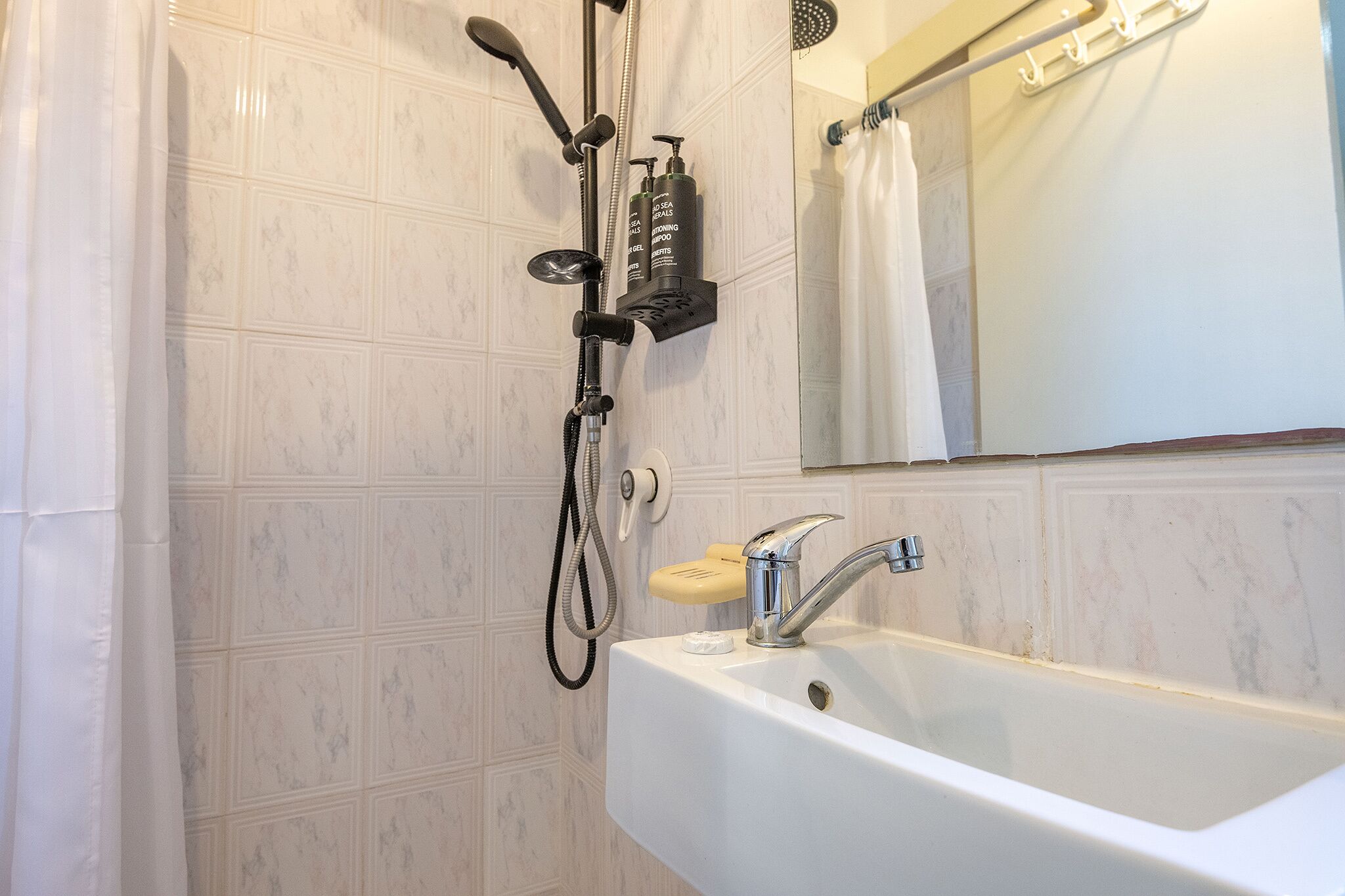 Ein Badezimmer mit einem weißen Waschbecken, einer Handbrause und einem hängenden Handtuchhalter.