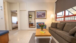 A living room with a sofa, a coffee table with a book and flowers, a TV, and a painting on the wall. - Mike's House Jerusalem (Jerusalem)