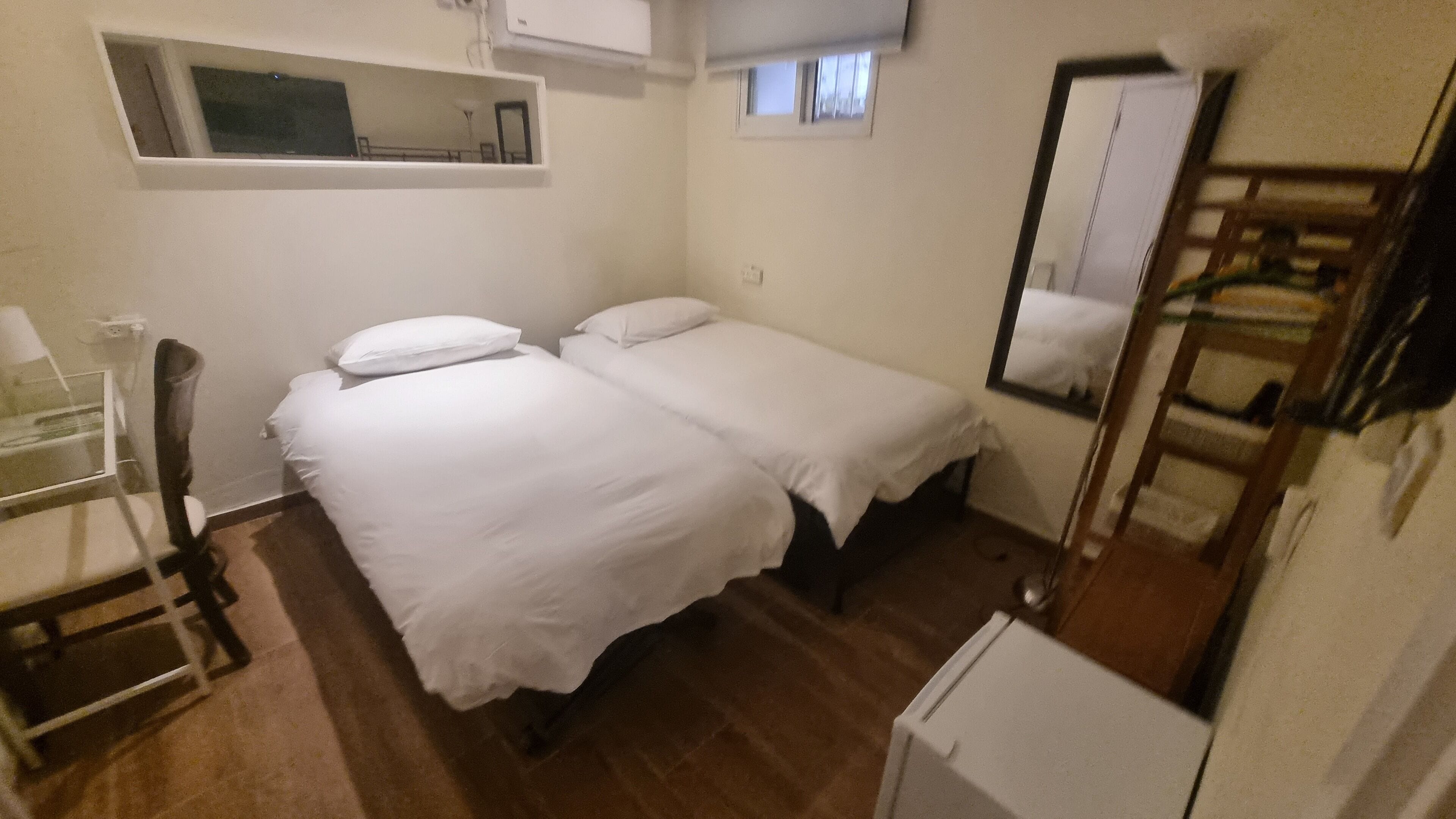A small, clean room with two single beds, a desk, and a mirror.
