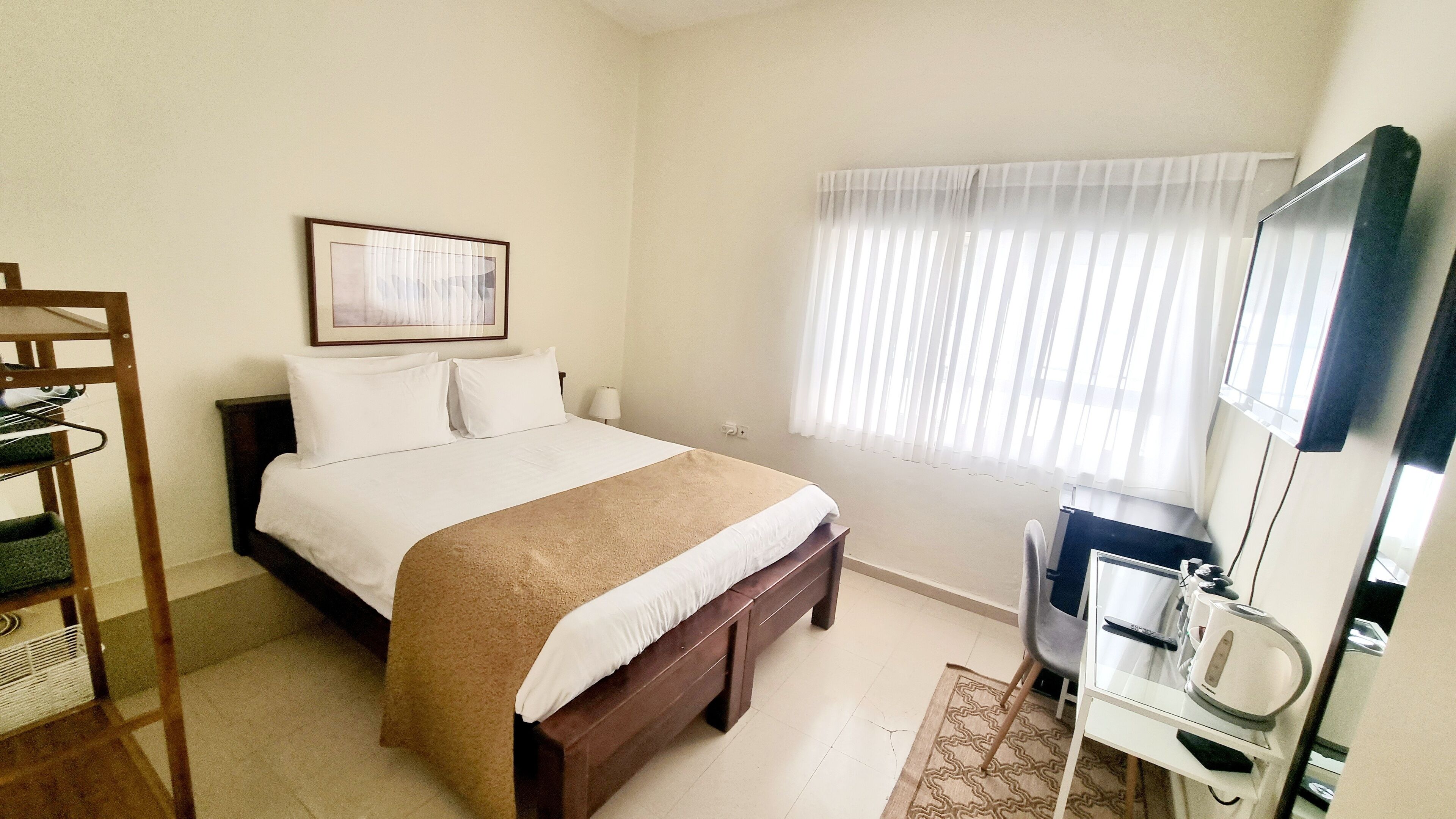 Habitación de hotel con cama, mesita de noche con lámpara, espejo y ventana con cortinas.