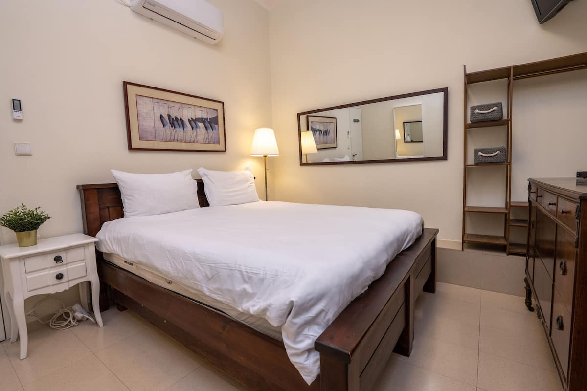 A neatly arranged bedroom with a wooden bed, bedside tables, a lamp, a mirror, and a wardrobe.