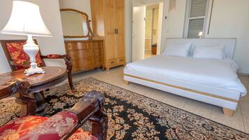 Un dormitorio con cama, armario de madera, espejo, mesita de noche con lámpara y una butaca tapizada en rojo.