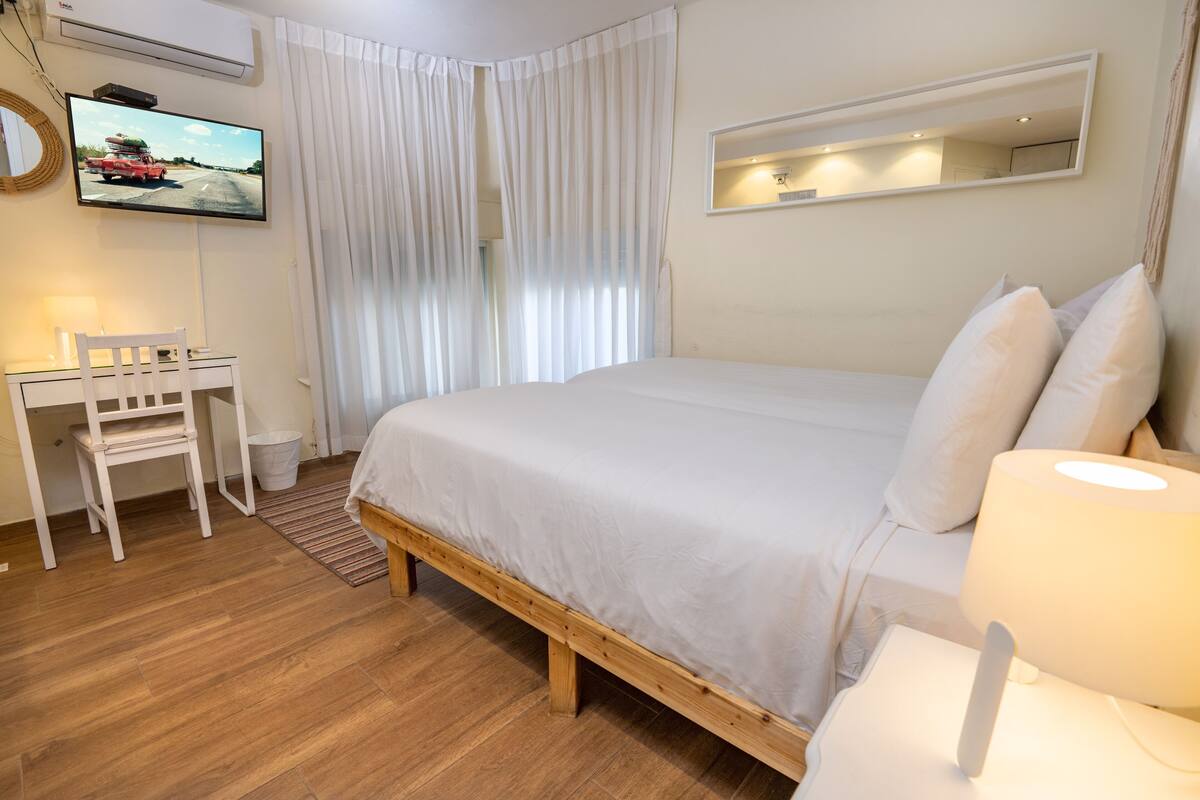 A hotel room with a bed, a desk, a chair, a television mounted on the wall, and a window with curtains.