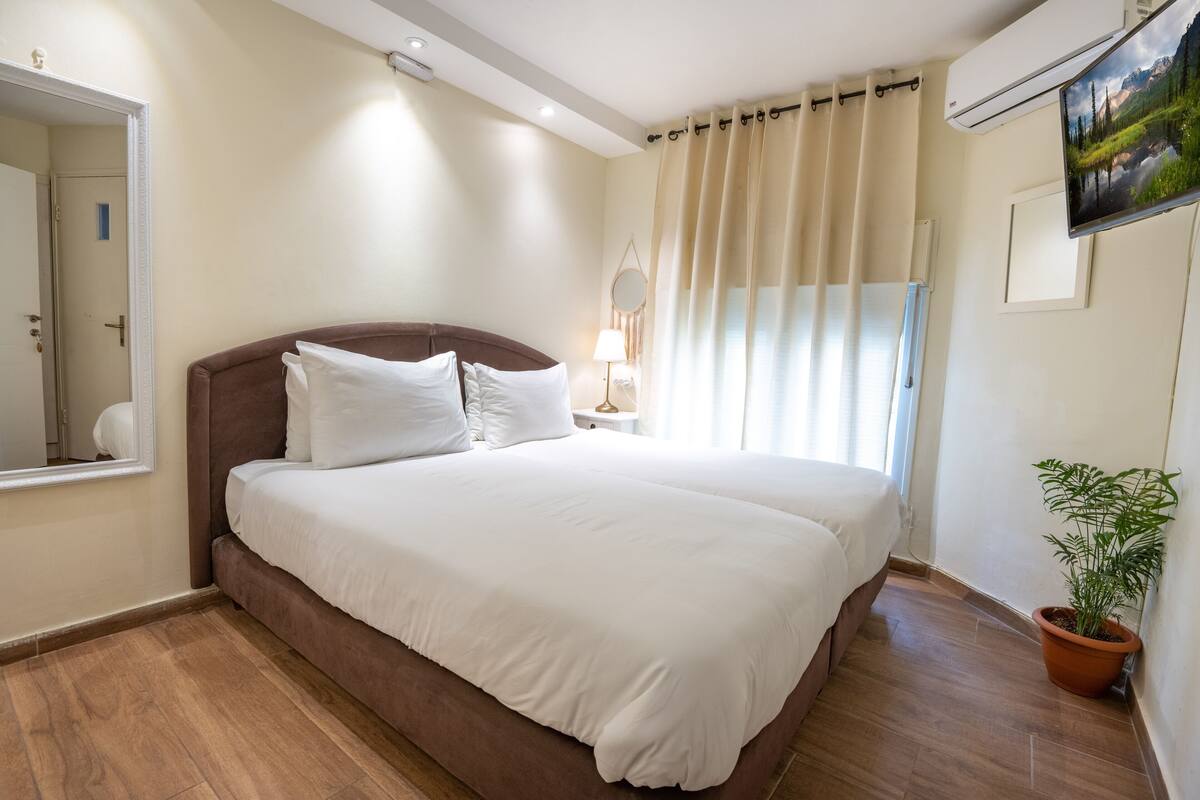 A neatly made bed with white linens, a brown headboard, and a bedside table with a lamp.