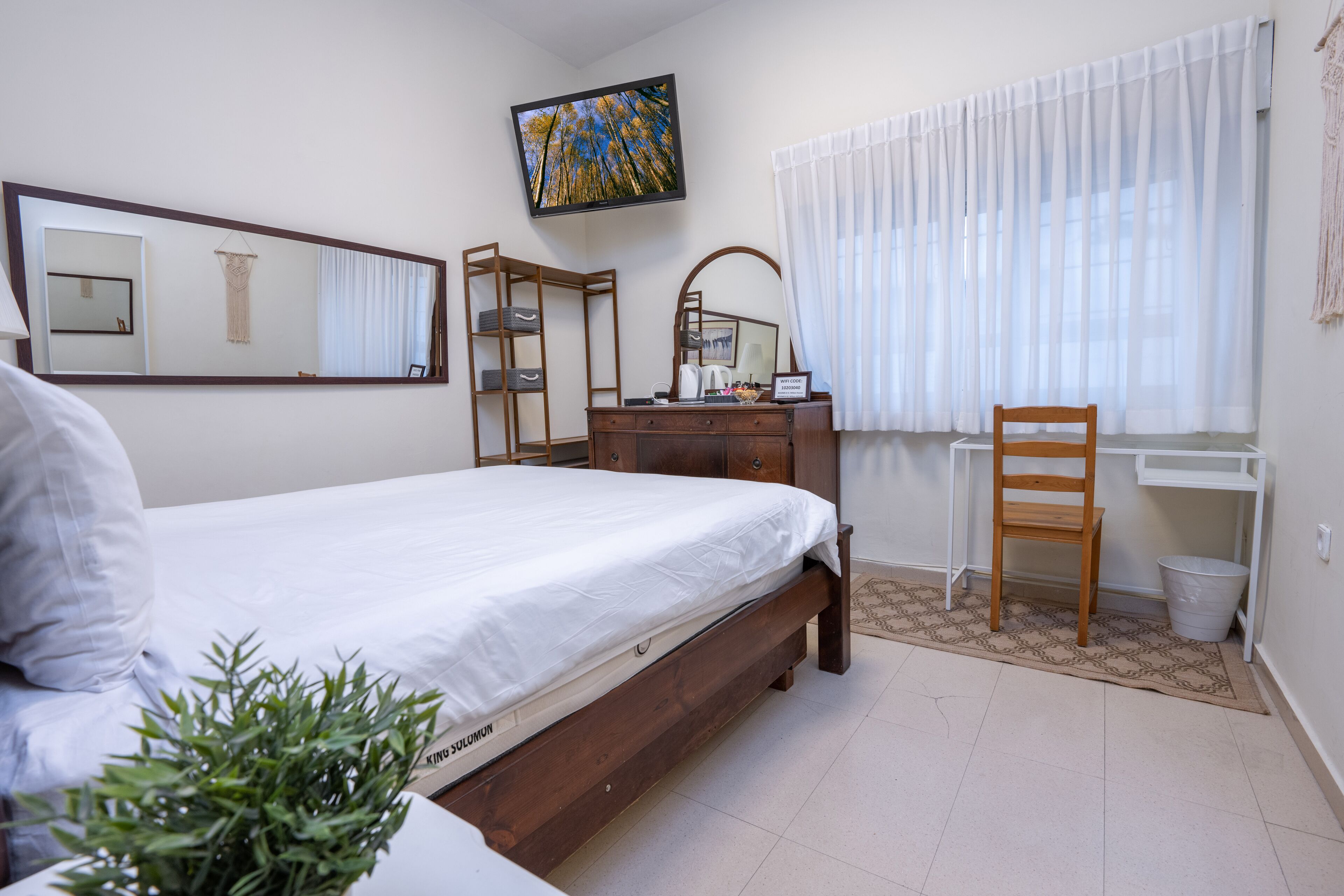 A hotel room with a bed, a desk, a chair, a mirror, and a television.