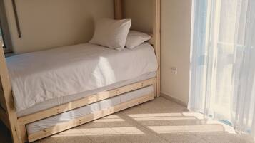 Una cama individual con ropa blanca, un espejo redondo en la pared y vistas al exterior a través de cortinas translúcidas.