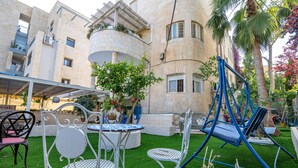 A courtyard with outdoor seating, a swing set, and a building with balconies and potted plants. - Mike's House Jerusalem (Jerusalem)