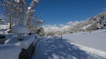 A snow-covered landscape with a stone wall, a lamp post, and a clear blue sky.