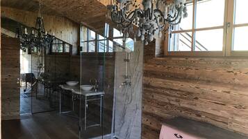 A wooden cabin interior with a modern bathroom featuring a glass shower enclosure, a marble sink, and a chandelier.