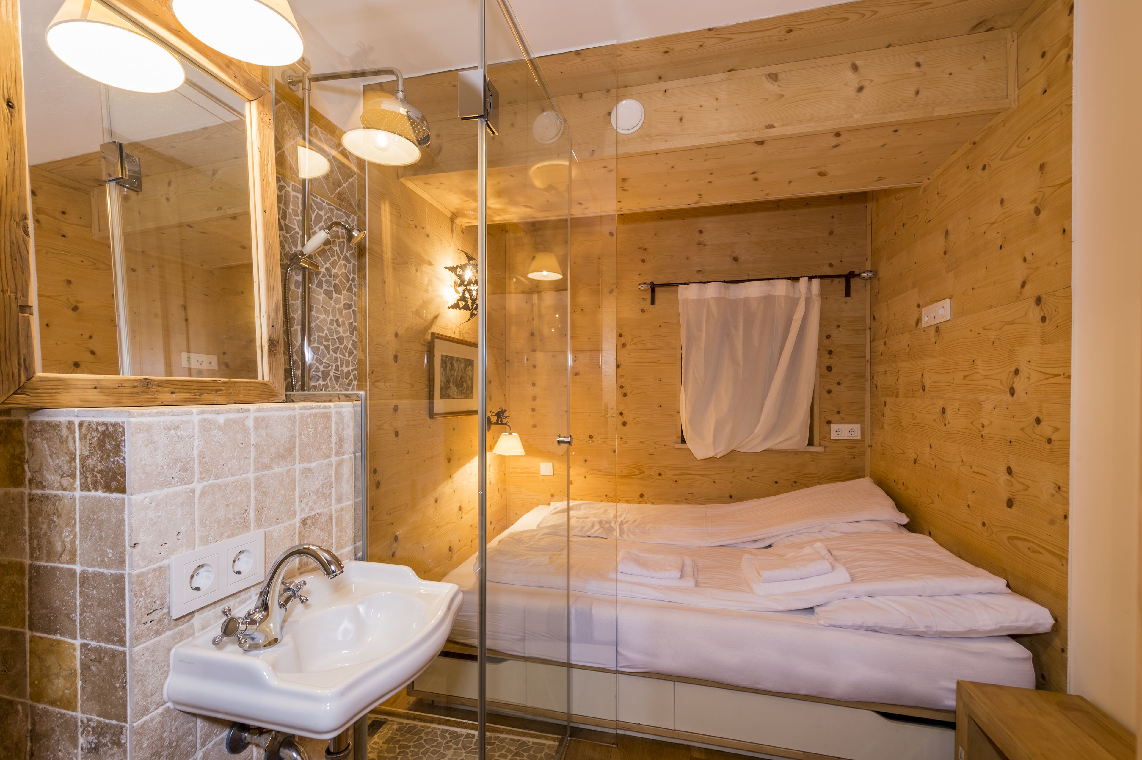 Una camera arredata in stile baita con doccia a vetro, un letto con lenzuola bianche e un bagno con lavandino e specchio.