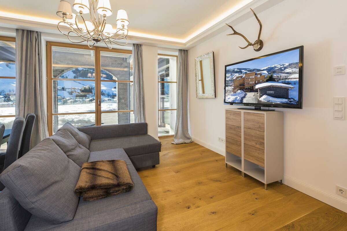 Uma sala de estar moderna com uma janela grande, um sofá cinza, piso de madeira, televisão e cabeça de veado montada.