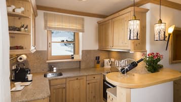 A kitchen with wooden cabinets, a granite countertop, a window with a view of a snowy landscape, a coffee machine, and a wine bottle.