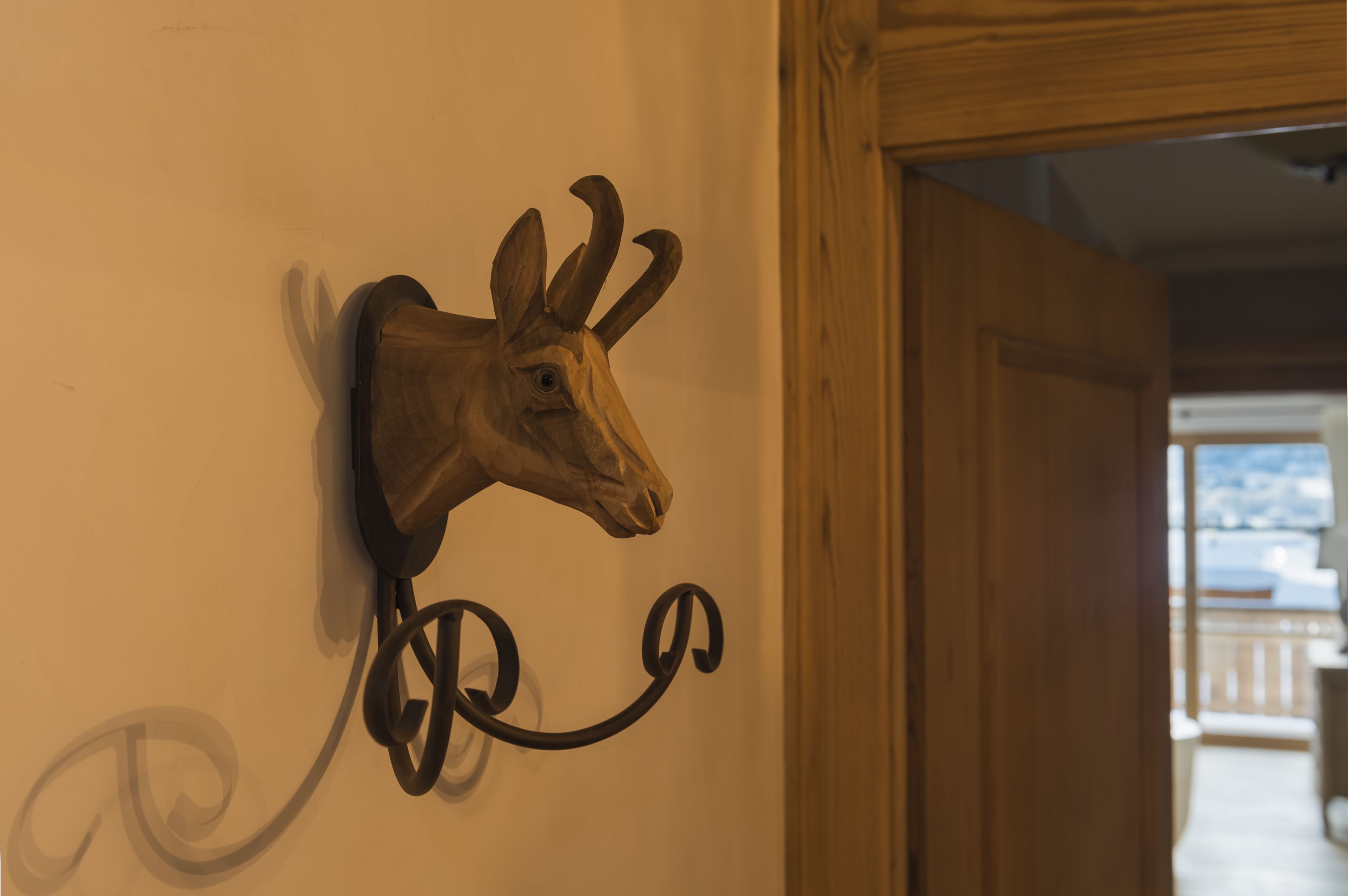 Une tête de cerf en bois, fixée au mur et ornée d’un motif décoratif en métal en forme de volute.